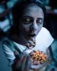 Hübsche Frau mit grau glitzernder Leuchtfarbe im Gesicht, die mit geschlossenen Augen Müsli isst. — Stockfoto