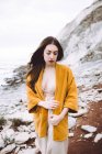 Brunette woman in bra and yellow jacket waking at coastline — Stock Photo