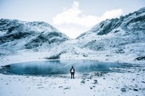 Indietro vista del turista in piedi sul lago ghiacciato in montagne innevate . — Foto stock
