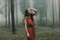 Jeune brunette en robe debout dans des bois effrayants — Photo de stock