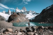 Indietro vista di backpacker in piedi a piccolo lago in montagne coperte di neve . — Foto stock