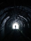 Creepy silhouette standing in tunnel with light in end. — Stock Photo