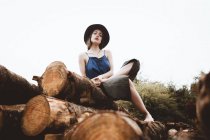 Stilvolle brünette Frau mit Hut posiert auf Baumstamm-Stapel — Stockfoto