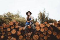 Stylish brunette woman in hat sitting on log pile — Stock Photo