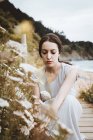 Zarte brünette Frau mit Blume an der Küste — Stockfoto