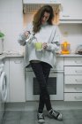 Брюнетка, стоящая на кухне и наливающая кофе из металлического горшка . — стоковое фото