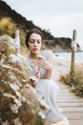 Tenera donna bruna con fiore in mano sulla costa — Foto stock