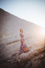 Vue latérale de la jeune brune en robe longue posant à la falaise — Photo de stock