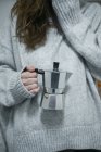 Кукурудзяна жінка в сірому светрі, що стоїть з металевим кавовим горщиком . — стокове фото