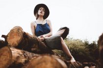 Brunette woman in hat sitting on log pile — Stock Photo