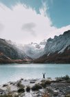 Distant view of tourist standing on hands at lake in mountains. — Stock Photo