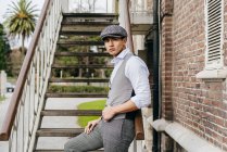 Cheerful man in vintage clothes and cap posing  on stairs — Stock Photo