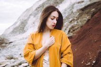 Young brunette in stylish jacket standing on shore and looking down gently. — Stock Photo