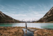 Back view of hiker with backpack standing at lake in mountains. — Stock Photo