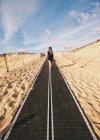 Back view of pretty woman on walkway placed in sand. — Stock Photo