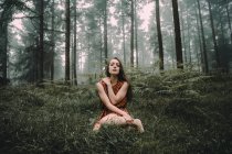 Брюнетка в платье сидит на лужайке в жутком лесу — стоковое фото