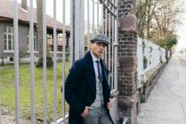 Stilvoller junger Mann lehnt am Tor und blickt auf der Straße in die Kamera. — Stockfoto