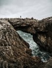 Side view of tourist standing on natural rock bridge at seaside. — Stock Photo