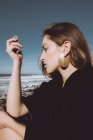 Chica joven en abrigo negro sentado en la costa y con guijarro en la mano - foto de stock