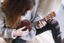 Кроп брюнетка женщина, играющая укулеле дома — стоковое фото