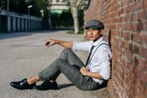 Homem elegante em boné vintage sentado na parede de tijolo — Fotografia de Stock