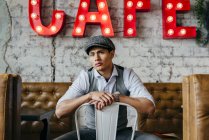 Man in cap posing on chair in cafe and looking at camera. — Stock Photo