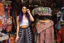Joven mujer asiática en gafas de sol de pie en la tienda de ropa . - foto de stock
