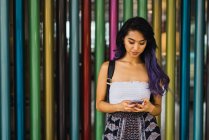 Jeune femme naviguant smartphone sur fond de colonnes colorées — Photo de stock