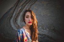 Brunette girl with red lips in dress against rock — Stock Photo