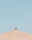Unbekannter Tourist steht an wolkenlosem Tag auf sandigem Hügel. — Stockfoto