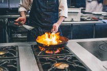Crop cook making flambe in restaurant kitchen — Stock Photo
