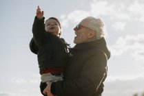 У віці чоловік носить онука в обіймах — стокове фото