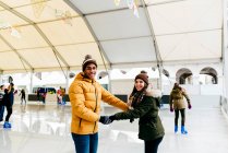 Cheerful young multiethnic couple holding hands while riding on skating rink. — Stock Photo