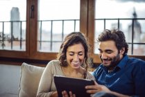 Smiling couple sitting on sofa and using tablet — Stock Photo