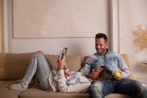 Young woman lying on knees of boyfriend and reading magazine on couch — Stock Photo