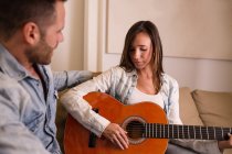 Woman playing guitar for boyfriend on coach at home — Stock Photo