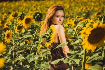 Hübsche junge Frau posiert auf Sonnenblumenfeld und blickt über die Schulter in die Kamera. — Stockfoto