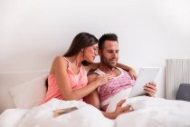 Paar mit Tablet im Bett umarmt — Stockfoto