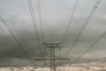Vista inferior de cables negros y poste de potencia de alto voltaje en el fondo del cielo nublado oscuro . - foto de stock