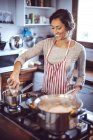 Sorridente bruna donna cucina il cibo sui fornelli — Foto stock