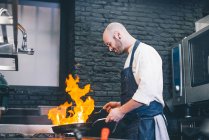 Cocinero haciendo flambe en cocina de restaurante - foto de stock