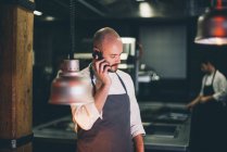 Шеф-повар разговаривает на смартфоне на кухне ресторана — стоковое фото