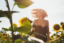 Молода жінка стоїть в соняшниках і трясе волосся — стокове фото