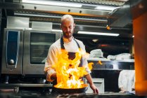 Chef standing in restaurant kitchen and making flambe on frying pan. — Stock Photo