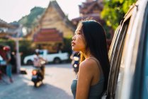 Young woman leaning on car at street scene — Stock Photo