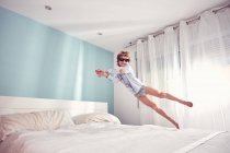 Jovem alegre se divertindo e pulando na cama em casa . — Fotografia de Stock