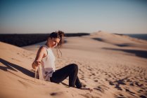 Seitenansicht einer hübschen Frau, die auf einer Düne sitzt und mit Sand spielt — Stockfoto