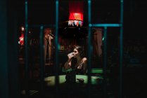 Giovane donna seduta e bere birra da sola nel bar vuoto di notte . — Foto stock