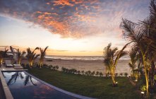 Vista para a bela praia de areia com palmas e gramado verde em luzes de pôr do sol . — Fotografia de Stock
