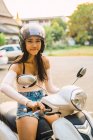 Молодая женщина сидит на скутере и смотрит в камеру — стоковое фото